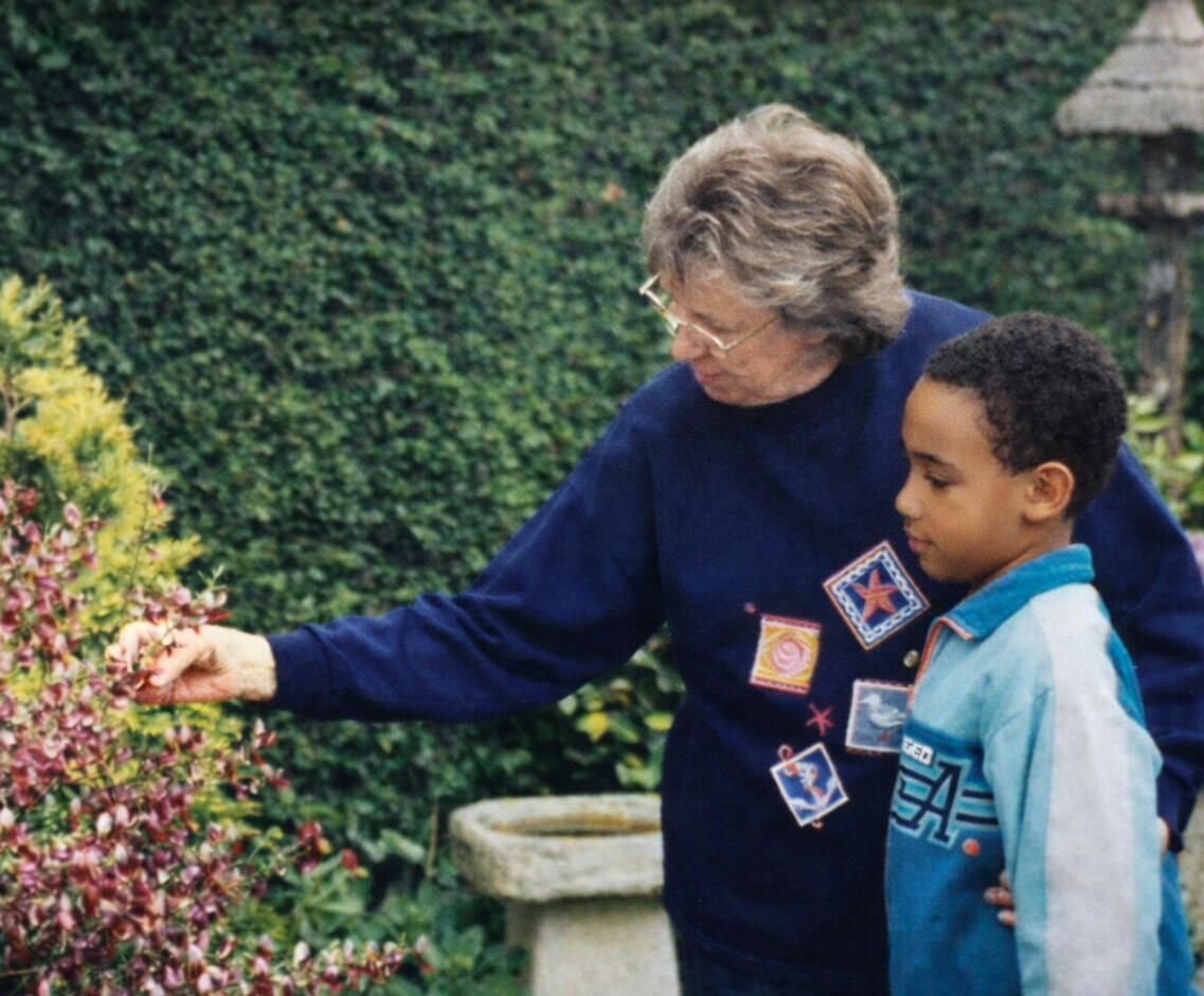 Restored photograph of Alexander J. Lynn, a UK-trained garden designer now based in North Carolina, as a child. He stands in a garden with his grandmother, her arm extended and her hand touching a native plant.
